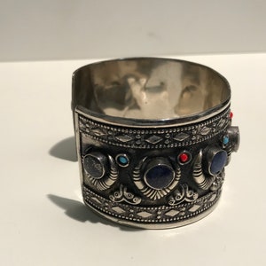 May include: Silver cuff bracelet with intricate designs and blue, red, and turquoise gemstones.