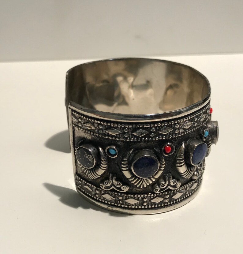 May include: Silver cuff bracelet with intricate designs and blue, red, and turquoise gemstones.