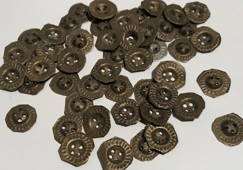 May include: A collection of antique brass-coloured buttons. The buttons have a decorative, octagonal shape with a textured rim and four holes for sewing. The buttons are scattered on a white surface.