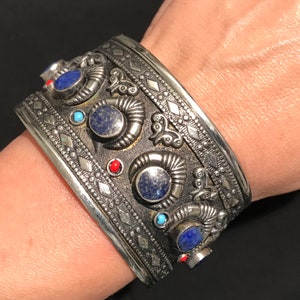 May include: A silver bracelet with intricate designs and blue and red gemstones.