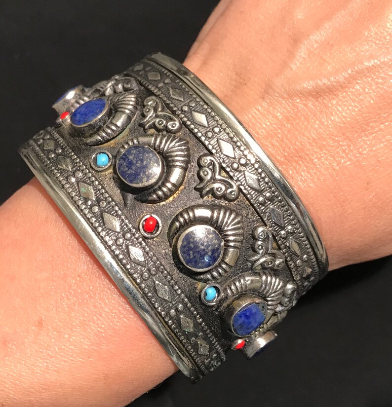 May include: A silver bracelet with intricate designs and blue and red gemstones.