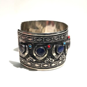 May include: Silver cuff bracelet with intricate detailing and blue and red gemstones.