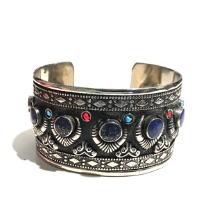 May include: A silver cuff bracelet with intricate designs and blue, red, and turquoise gemstones.