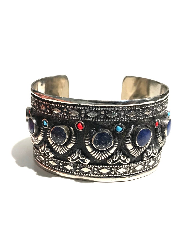 May include: A silver cuff bracelet with intricate designs and blue, red, and turquoise gemstones.