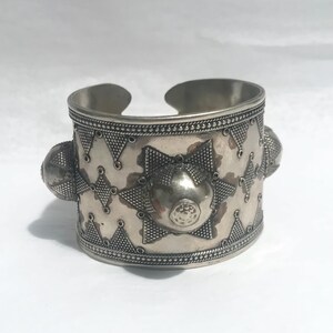 Op de afbeelding: Een zilveren armband met een geometrisch patroon en drie verhoogde, ronde accenten. De armband is gemaakt van metaal en heeft een glanzende afwerking.