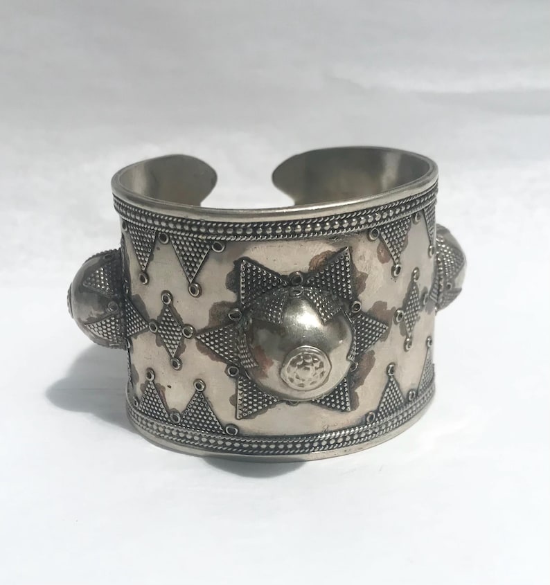 Op de afbeelding: Een zilveren armband met een geometrisch patroon en drie verhoogde, ronde accenten. De armband is gemaakt van metaal en heeft een glanzende afwerking.