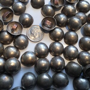 May include: A large collection of silver-toned metal dome-shaped buttons with a raised center. The buttons have a smooth, shiny finish.