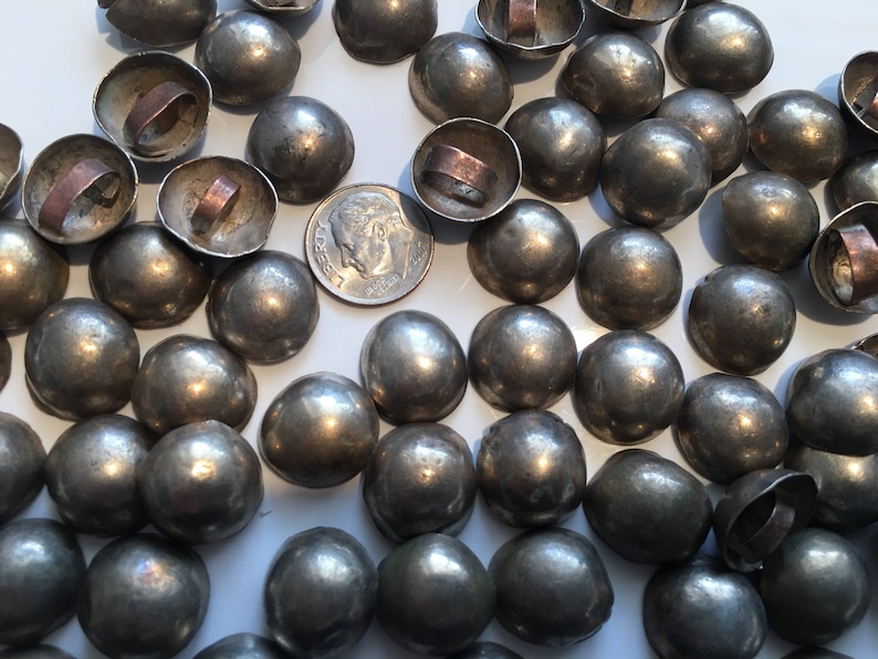 May include: A large collection of silver-toned metal dome-shaped buttons with a raised center. The buttons have a smooth, shiny finish.