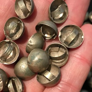 May include: A close-up of a pile of silver-toned dome-shaped buttons with a metal ring around the top. The buttons are about 1 inch in diameter.