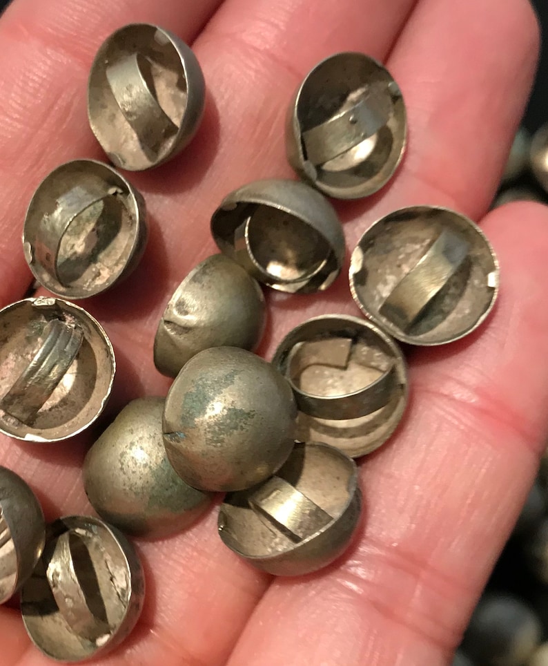 May include: A close-up of a pile of silver-toned dome-shaped buttons with a metal ring around the top. The buttons are about 1 inch in diameter.