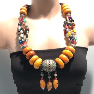 Puede incluir: Un collar de múltiples hilos con grandes cuentas de ámbar y un colgante de plata con esmalte azul y verde. El collar está hecho de varios materiales, incluyendo ámbar, plata y cuentas de vidrio.