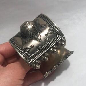 Op de afbeelding: Een zilveren armband met ingewikkelde geometrische ontwerpen en een gewelfde bovenkant. De armband is gemaakt van metaal en heeft een getextureerd oppervlak.