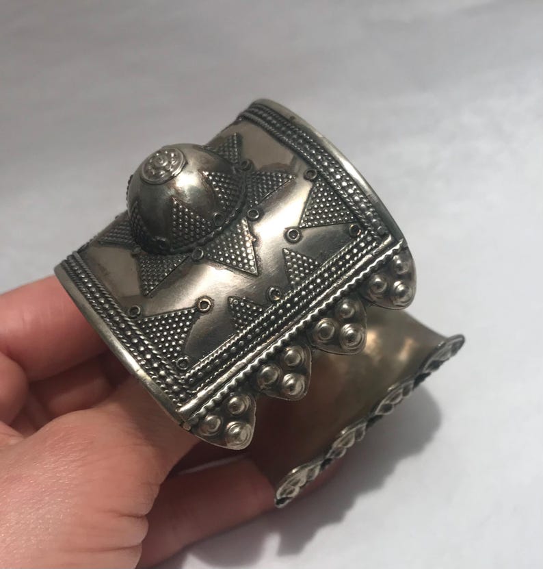 Op de afbeelding: Een zilveren armband met ingewikkelde geometrische ontwerpen en een gewelfde bovenkant. De armband is gemaakt van metaal en heeft een getextureerd oppervlak.
