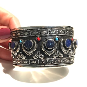May include: A silver cuff bracelet with intricate designs and blue and red gemstones.
