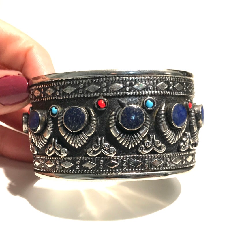 May include: A silver cuff bracelet with intricate designs and blue and red gemstones.