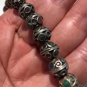 May include: A silver bracelet with round beads, each bead is decorated with a silver filigree design and inlaid with small turquoise, red, and blue stones.