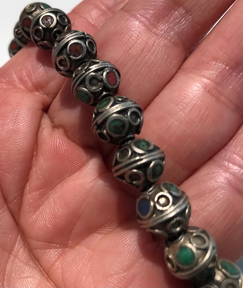 May include: A silver bracelet with round beads, each bead is decorated with a silver filigree design and inlaid with small turquoise, red, and blue stones.