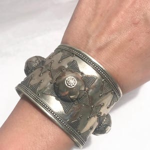 Op de afbeelding: Een zilveren armband met een geometrisch ontwerp en meerdere ronde accenten. De armband is breed en heeft een getextureerd oppervlak.