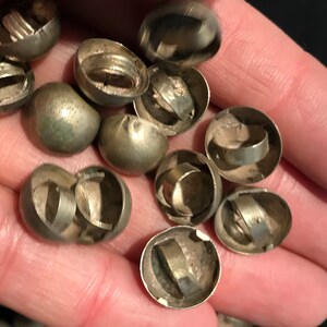 May include: A close-up of a pile of silver-colored metal bells. The bells are round and have a small opening at the top. They are all open and show the inside of the bell.