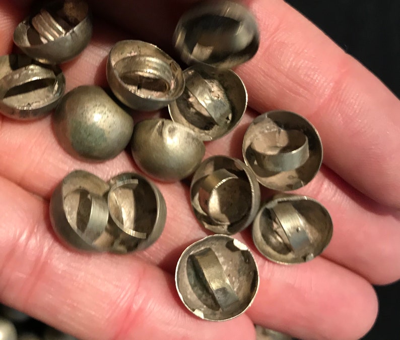 May include: A close-up of a pile of silver-colored metal bells. The bells are round and have a small opening at the top. They are all open and show the inside of the bell.
