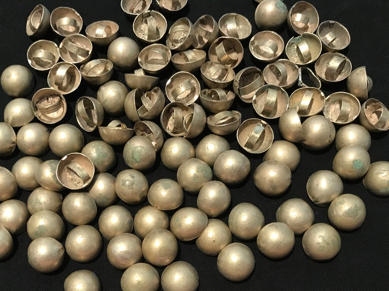 May include: A large group of silver-toned metal dome-shaped buttons with a ring on the top. The buttons are scattered on a black surface.