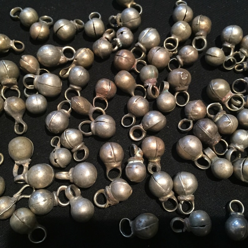 May include: A collection of silver-toned jingle bells with a rounded shape and a small loop at the top. The bells are scattered on a black surface.