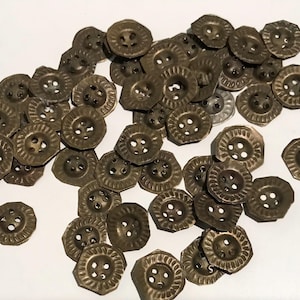 May include: A pile of antique brass-coloured buttons. Each button features a decorative, ridged edge and four holes for sewing. The buttons are scattered on a white surface, highlighting their aged appearance and intricate design.