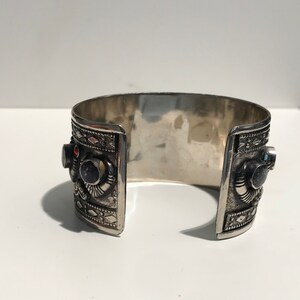 May include: A silver cuff bracelet with intricate designs and colorful gemstones. The bracelet is open on one side and has a hinged closure on the other.