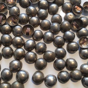 May include: A collection of silver-toned metal dome-shaped buttons with a ring on the top. The buttons are scattered on a white surface.