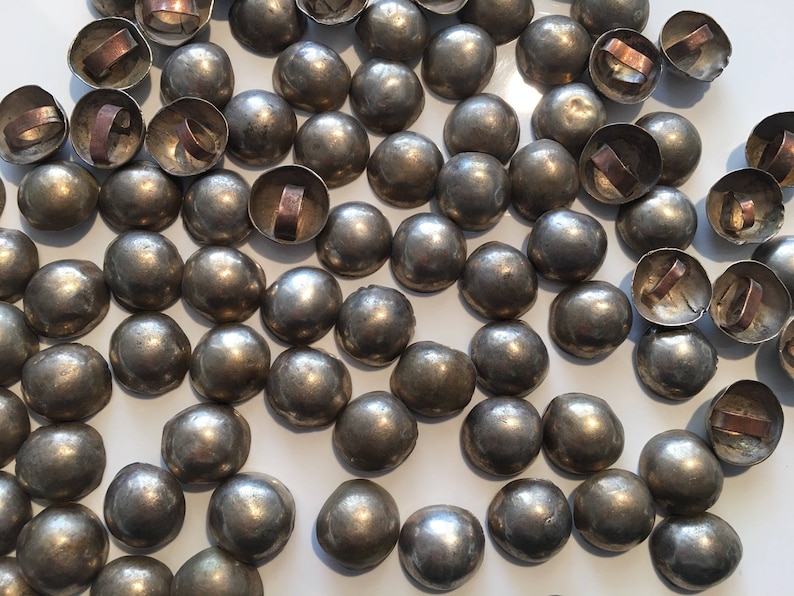 May include: A collection of silver-toned metal dome-shaped buttons with a ring on the top. The buttons are scattered on a white surface.