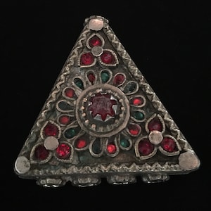 May include: A silver triangular box with red and green gemstones. The box has a decorative design around the edges and a floral pattern in the center.