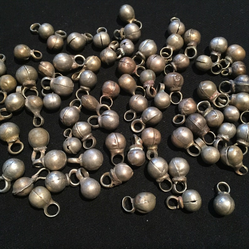 May include: A collection of silver jingle bells with a loop for hanging. The bells are all different sizes and shapes, and some have a slightly hammered finish.
