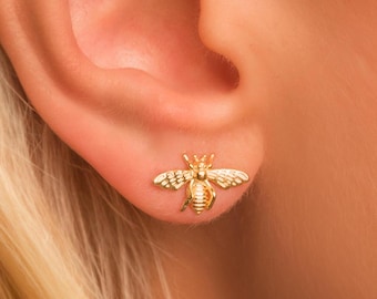 May include: Gold bee stud earrings. The bee is detailed with wings, legs, and a stinger.