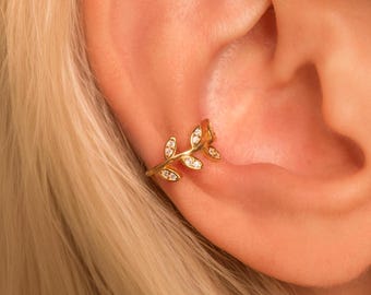 May include: Gold ear cuff with a leaf design and clear rhinestones. The cuff is worn on the upper part of the ear.