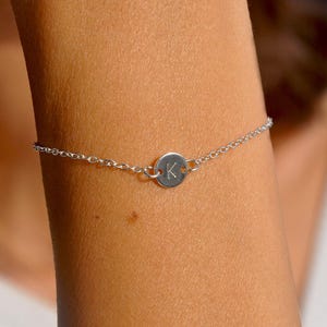 Peut inclure: Un bracelet en argent délicat avec un petit charme rond gravé de la lettre "K". Le charme est relié à une fine chaîne, créant un design minimaliste et élégant. Ce bracelet personnalisé est un accessoire élégant.