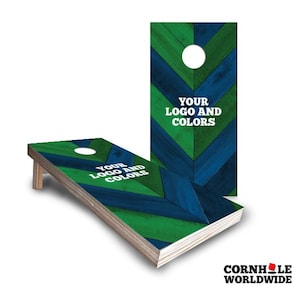 May include: Two cornhole boards featuring a chevron pattern in alternating dark blue and green wood grain textures. Each board has a circular hole at the top and the white text "YOUR LOGO AND COLORS" printed in the center of the playing surface.