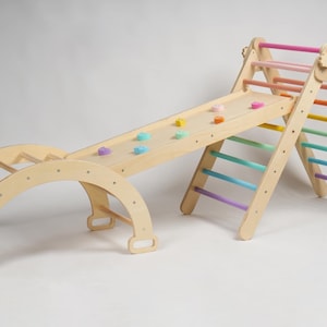 May include: Wooden playset with a slide, climbing wall, and ladder. The slide has a rainbow of colors and the climbing wall has a rainbow of colors. The ladder has a rainbow of colors.