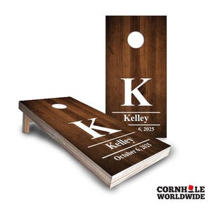 May include: A set of two wooden cornhole boards with a brown woodgrain finish. The boards have a white letter "K" and the name "Kelley" with a date.