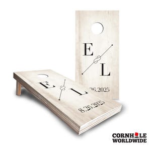 May include: Two light-colored wooden cornhole boards featuring a white-washed wood grain finish. Each board displays the black letters E and L separated by a thin line with a knot graphic, and the date 8.26.2025 printed in black at the bottom.