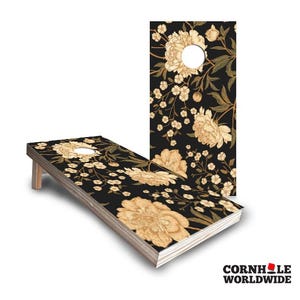 May include: A set of two cornhole boards with a floral design. The boards are black with a white floral pattern. The boards are made of wood and have a brown stain.
