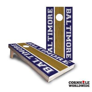 May include: A set of two cornhole boards with a blue and gold design. The boards feature the word "Baltimore" in white lettering on a blue background with a gold stripe.