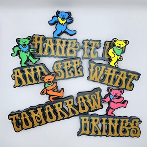 May include: Colorful wooden cutouts featuring dancing bears and the phrase "Hang It And See What Tomorrow Brings" in gold lettering. The bears are in various colors, including blue, green, yellow, orange, and pink.