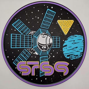 May include: A round, black graphic featuring a space theme. It includes a satellite with solar panels, a blue planet, a yellow triangle, and the text "STSS" in purple and gold. The border is purple, and white dots represent stars.