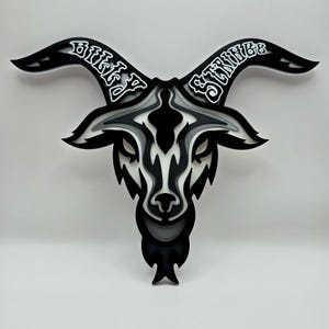 May include: A layered goat head design in black, white, and gray. The artwork features the text "Billy Strings" in white, arched across the horns. The design has a three-dimensional effect, with multiple layers creating depth and shadow.