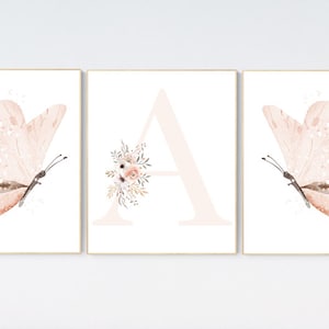 Puede incluir: Tres impresiones de acuarela que representan una mariposa rosa, la letra A con acentos florales y otra mariposa rosa. Las impresiones est&aacute;n enmarcadas en un marco de madera claro.