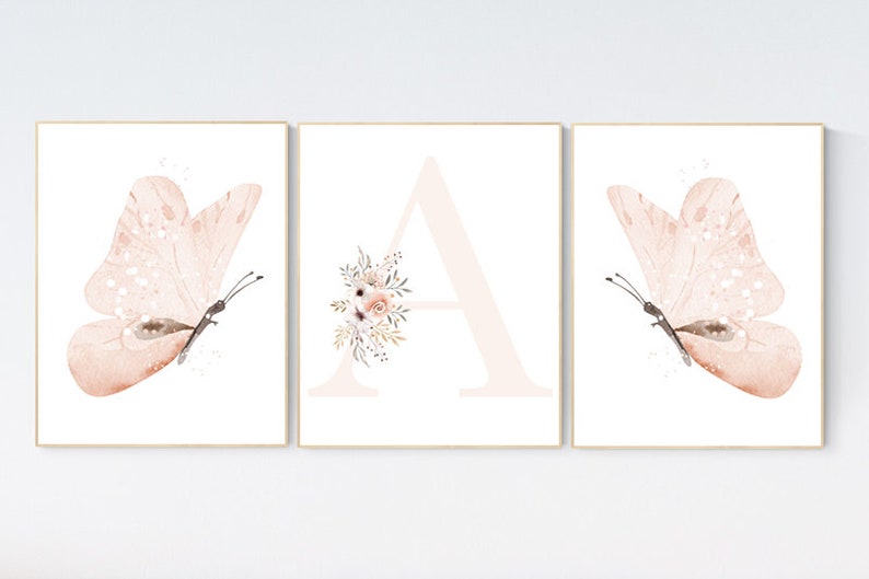 Puede incluir: Tres impresiones de acuarela que representan una mariposa rosa, la letra A con acentos florales y otra mariposa rosa. Las impresiones est&aacute;n enmarcadas en un marco de madera claro.
