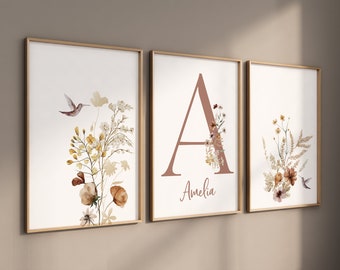 May include: Three framed art prints with botanical illustrations. One print features a hummingbird and floral arrangement in shades of yellow, brown, and white. Another displays the letter "A" with floral accents and the name "Amelia". The third print has a hummingbird and floral arrangement.
