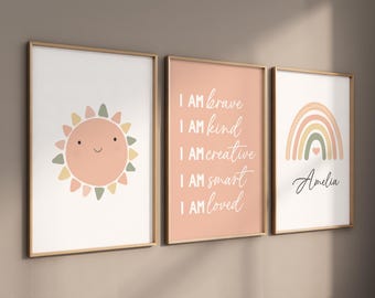 May include: Three framed prints with a peach background. The left print features a smiling sun with peach, green, and yellow accents. The middle print has the text "I AM brave I AM kind I AM creative I AM smart I AM loved" in white. The right print has a rainbow with peach, green, and yellow accents and the text "Amelia" in black.