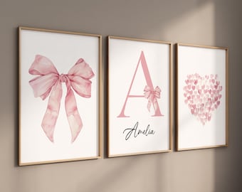 May include: Three framed prints with a pink watercolor bow, a pink watercolor letter A with the name Amelia, and a pink watercolor heart made of smaller hearts.