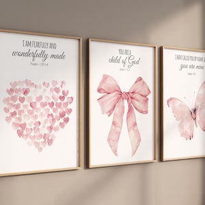 Pode incluir: Três impressões emolduradas com ilustrações de aquarela rosa e citações inspiradoras. A primeira impressão apresenta um coração feito de corações rosas com a citação "Sou feito de maneira maravilhosa e temível" e a referência bíblica "Salmo 139:14". A segunda impressão apresenta um laço rosa com a citação "Você é um filho de Deus" e a referência bíblica "João 1:12". A terceira impressão apresenta uma borboleta rosa com a citação "Eu te chamei pelo seu nome e você é meu" e a referência bíblica "Isaías 43:1".